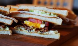 A close-up view of a sliced sandwich with layers of bacon, egg, lettuce, and tomato.